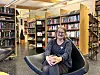 Kvinne sitter i stol foran bokhyller i et bibliotek